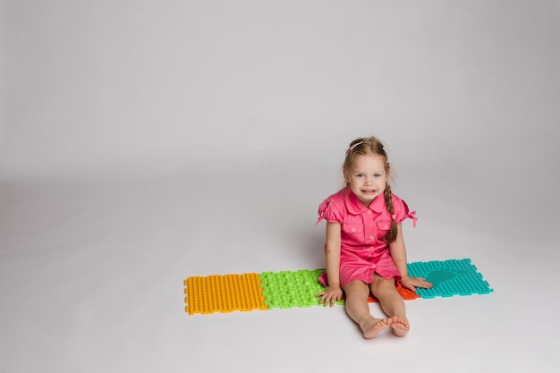 Free photo stock photo of a child playing with colorful bright rubber pads for improving and developing fine motor skills on the floor she is sitting on her haunches in studio