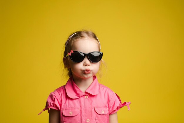 Stock photo portrait of adorable little kid in fashionable black sunglasses pouting her lips funnily on yellow background Isolate