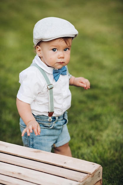 Free Photo stock photo portrait of a cutie in hat , shirt, shorts and bow with suspenders looking at camera while walking on green lawn in the backyard. looking at camera with curiosity.