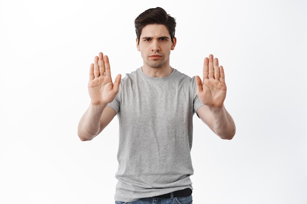 Stop it, keep distance. Serious frowning man showing block refusal gesture, stretch out hands to reject or decline something, prohibit action, standing over white background