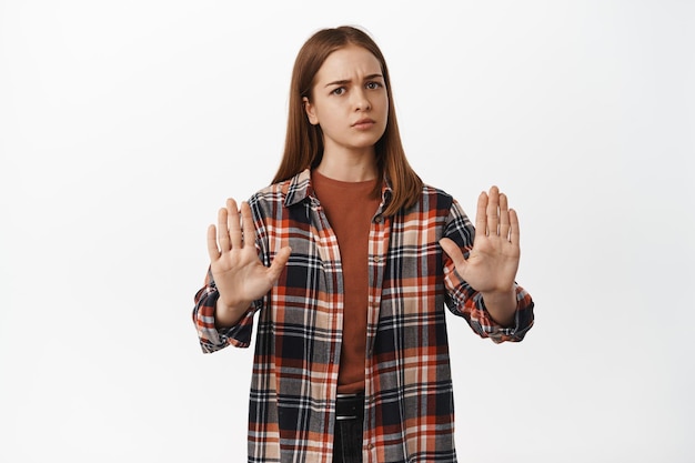 Free photo stop, slow down. upset young woman blocking, say no, rejecting smth bad, raising hands in block taboo gesture, dislike something bad and refusing it, white background