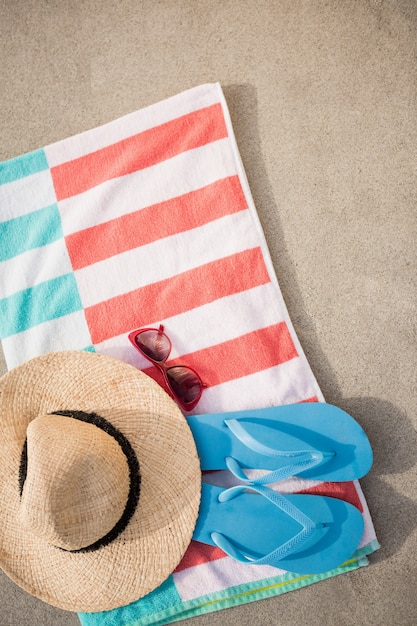 Free photo straw hat, blue flip flop and sunglasses kept on beach blanket