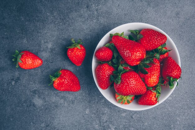 Strawberries in a bowl on a gray textured background. top view.