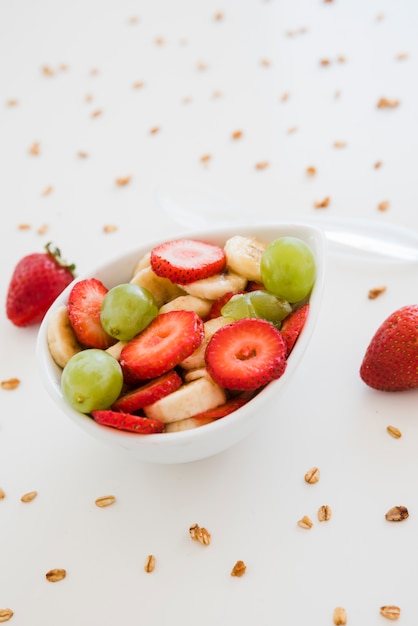 Strawberries; grapes and banana slices in bowl spread with oats on white backdrop