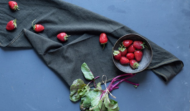 Strawberries inside bowl and leaves on a black mat. 