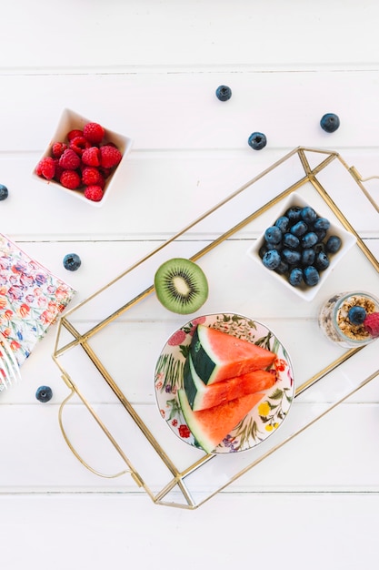 Free photo strawberries near slices watermelon; kiwi; blueberries and oats on tray