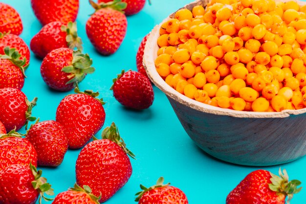 Strawberries and ripe sea-buckthorn berries on turquoise backdrop