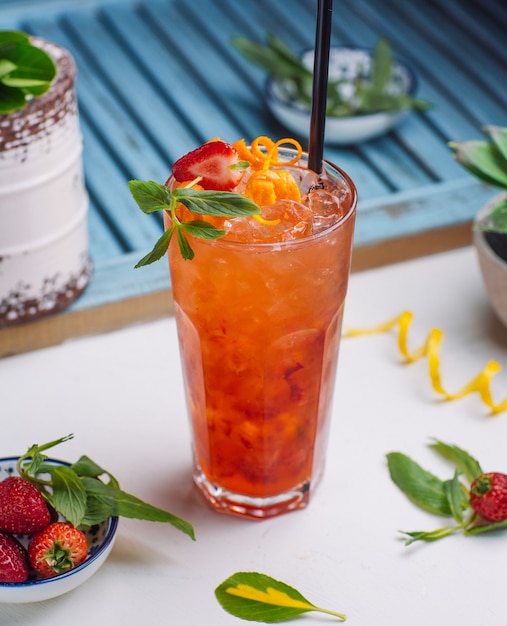 strawberry and orange juice with ice cubes, orange zest, strawberry piece in glass