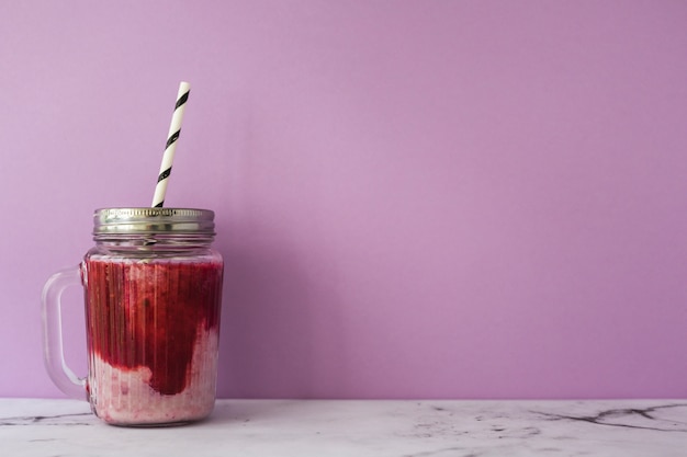 Strawberry smoothie in jar with closed lid and drinking straw against pink background