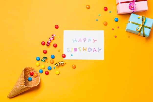 Free photo streamers and gems on waffle with happy birthday on paper against yellow background