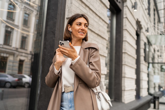 Street lifestyle portrait of stylish european business brunette woman in leather coat posing outdoor