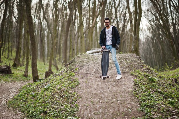 Street style arab man in eyeglasses with longboard on wood