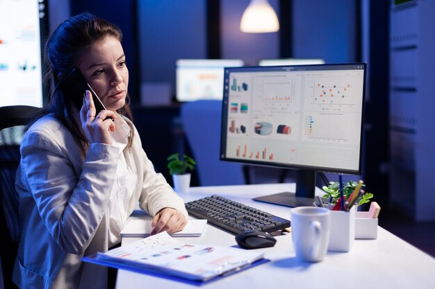 Stressed manager talking at smartphone with employee, working on financial problems before deadlines, sitting at desk in business office