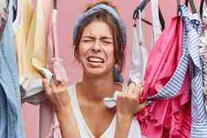 Free photo stressed unhappy young european female touching stylish clothes and crying out loud because she can't afford any of them. frustrated woman having sad and painful look as she has nothing to wear