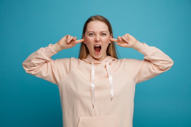 Stressed young blonde woman putting fingers in ears screaming 