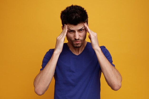 Stressed young handsome man looking at camera keeping hands on head on yellow background