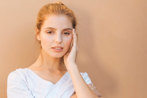 Free photo stressful young woman with her hand on face against beige background