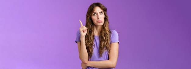 Strict funny curlyhaired girl pulling disappointed angry face popping eyes stare camera shaking index finger disapproval scold bad behaviour stand serious bossy purple background