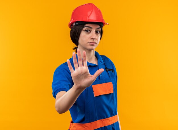 Strict looking at camera young builder woman in uniform showing stop gesture 