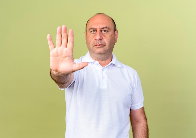 Strict mature man showing stop gesture isolated on olive green wall