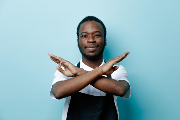 Strict showing gesture of no young african american barber in uniform isolated on blue background