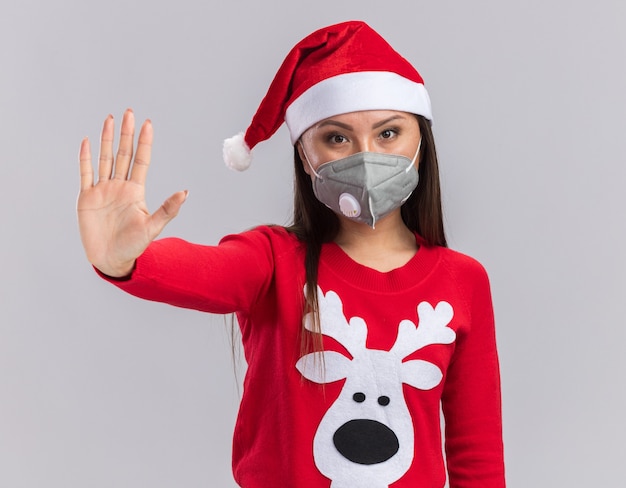 Free photo strict young asian girl wearing christmas hat with sweater and medical mask showing stop gesture isolated on white background