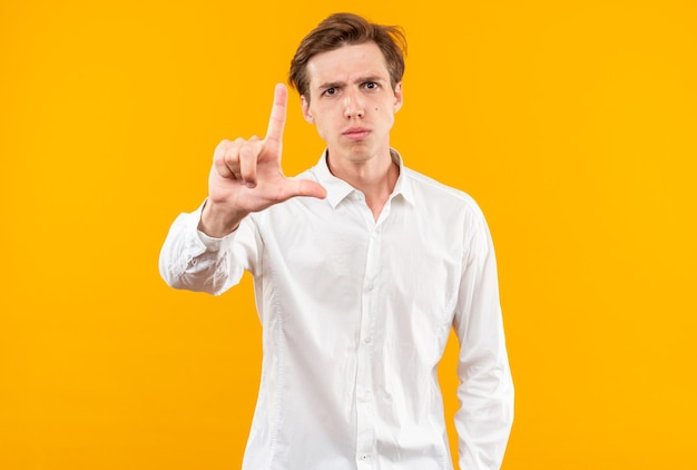 Strict young handsome guy wearing white shirt showing loser gesture isolated on orange wall