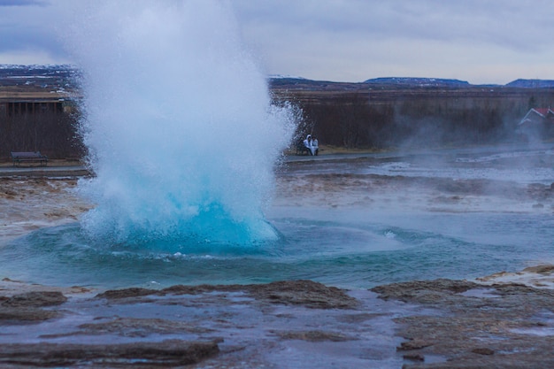 Free photo strokkur geyser surrounded by hills under a cloudy sky in the evening in iceland