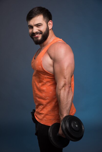 Strong man holding a dumbbell on dark blue wall.