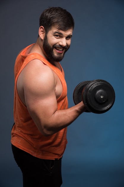 Strong man holding a dumbbell on dark blue wall.