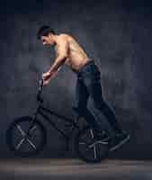 Free photo strong shirtless man, makes an acrobatic figure with bmx in a studio. isolated on a dark background.