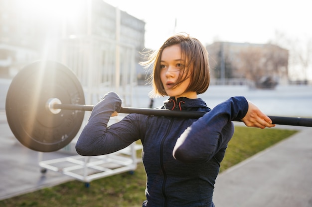 Strong woman exercising with barbell. Cute girl preparing for weightlifting workout. Sports, fitness concept.