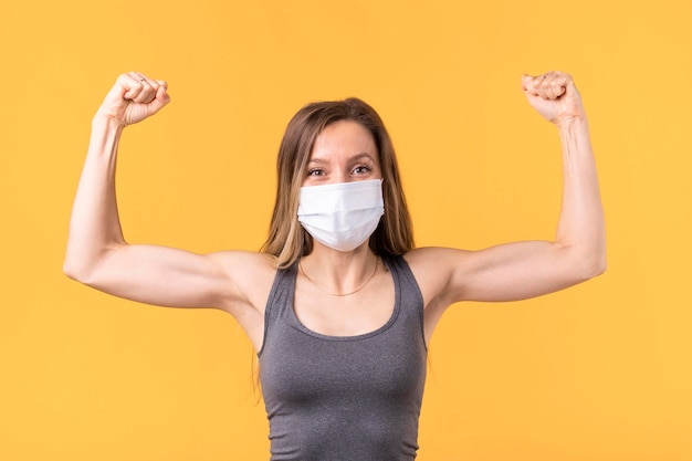 Free Photo strong woman with medical mask showing her muscles