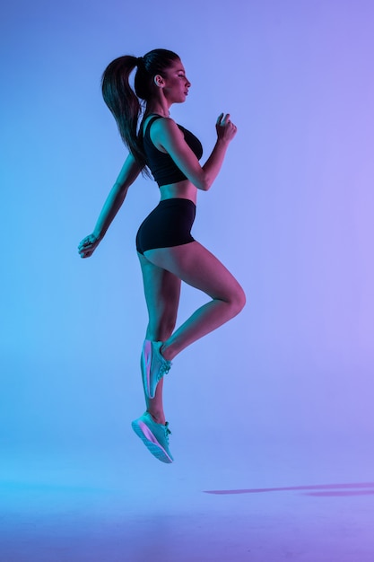 Strong young sports woman jump isolated over purple wall.