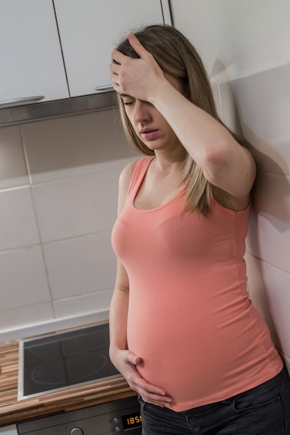 Struggling with morning sickness. Depressed pregnant woman holding hand on head and keeping eyes closed. Problems, sad, depression woman.