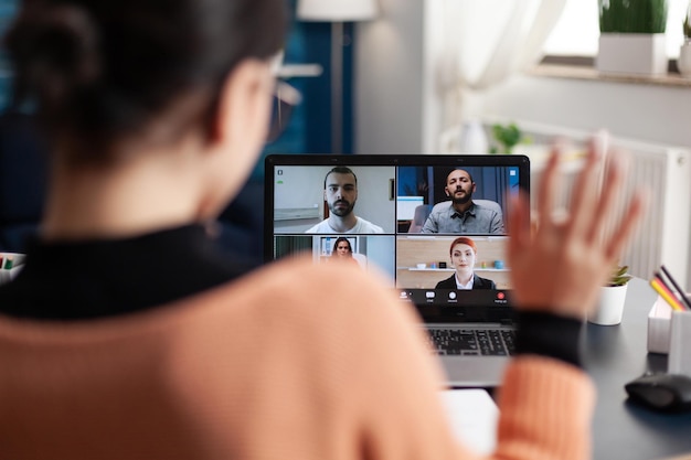 Free Photo student in a group videocall on laptop. freelancer working from home office meeting colleagues online. colleague waving at screen in webcam team conference. remote briefing conversation.