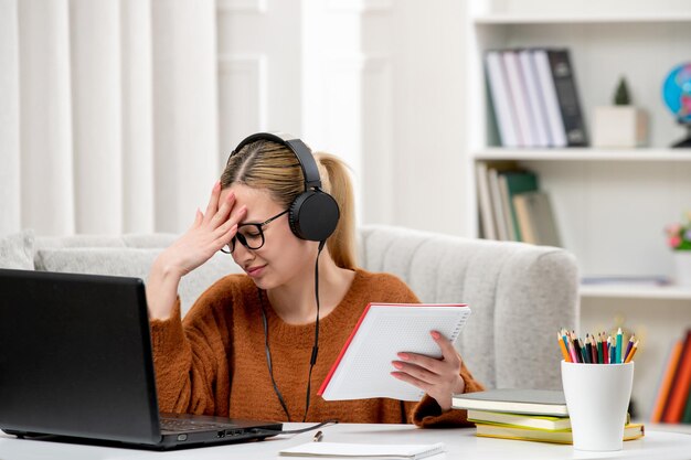 Student online cute girl in glasses and sweater studying on computer confused holding head