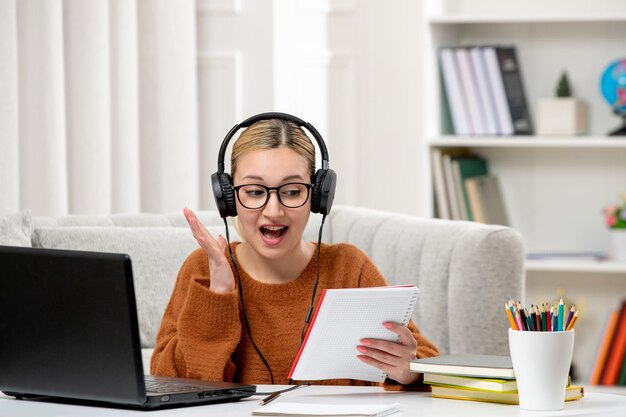 Student online cute girl in glasses and sweater studying on computer excited about her notes