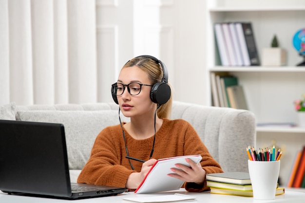 Student online cute girl in glasses and sweater studying on computer writing notes