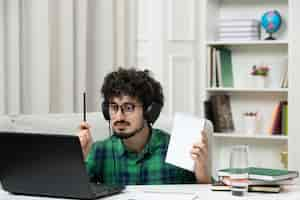 Free photo student online cute young guy studying on computer in glasses in green shirt holding pen notepad