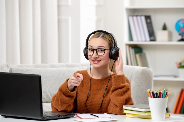 Student online young cute girl in glasses and orange sweater studying on computer pointing at front