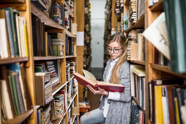 Free photo student reading book between bookcases