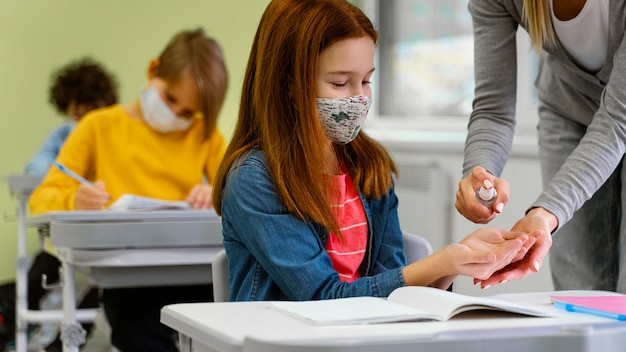 Free photo student with medical mask getting hand sanitizer from teacher