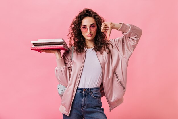 Student woman in pink sunglasses holding books and showing thumb down