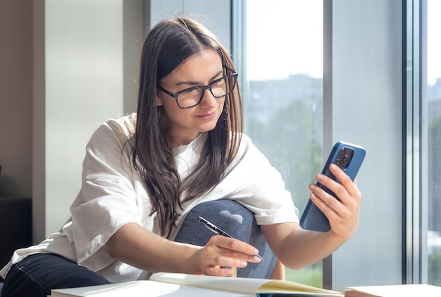 Free photo student woman with smartphone and notepads at the window in the morning