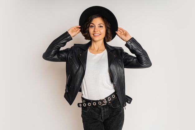 Free photo studio fashion photo of stylish brunette woman in black hat and leather jacket posing on white