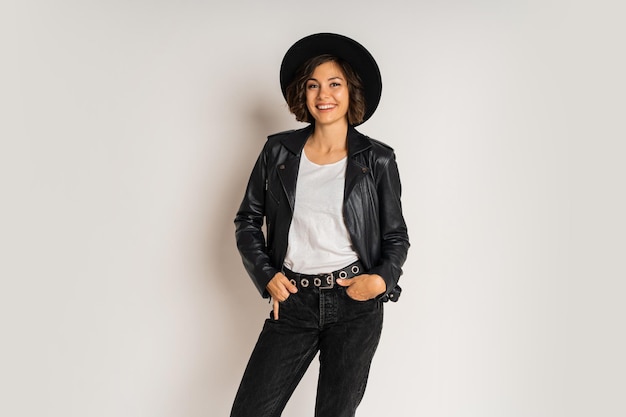 Free photo studio fashion photo of stylish brunette woman in black hat and leather jacket posing on white