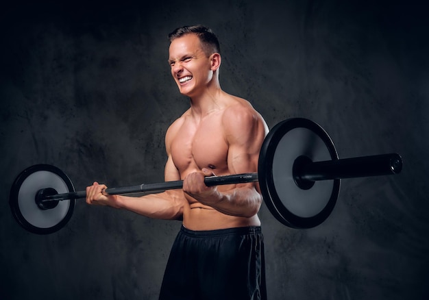 Studio image of shirtless muscular male holds barbell over grey vignette background.