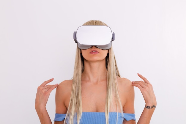 Studio photo of a young attractive woman in a warm blue fashionable suit wearing virtual reality glasses on a white