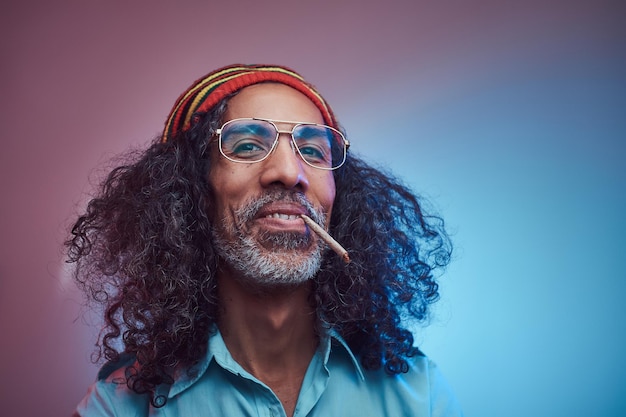 Studio portrait of African Rastafarian male smoking cigarettes. Isolated on a blue background.